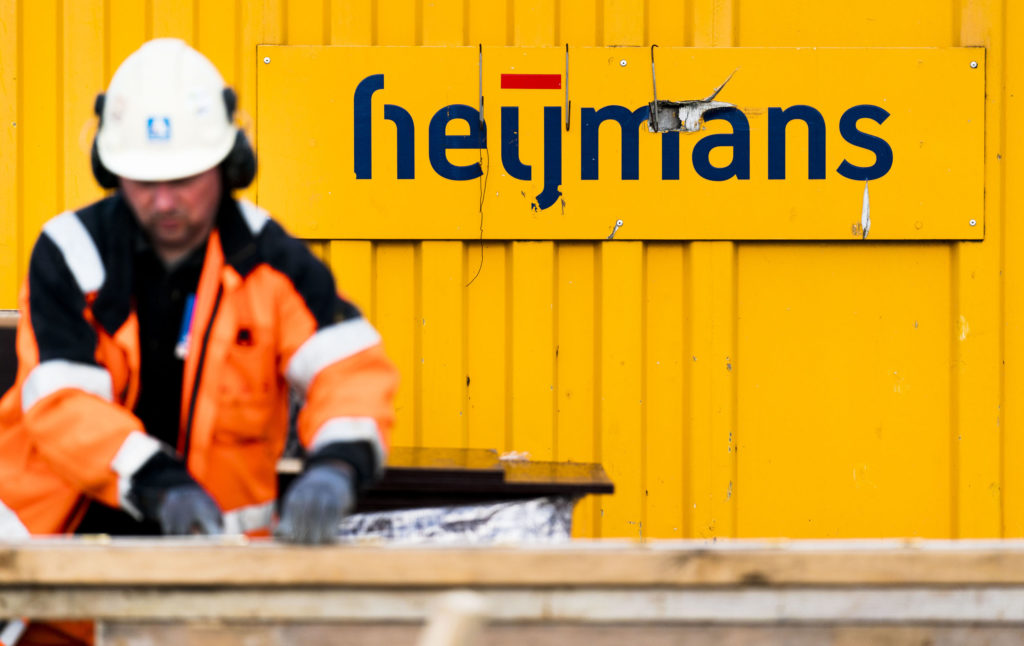 in de achtergrond het heijmans logo op een gele containerwand. op de voorgrond een man in heijmans werkkleding