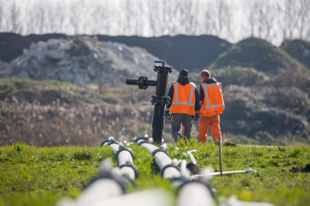 twee personen in het veld met oranje hesjes aan